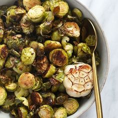 a bowl filled with brussel sprouts next to a golden spoon on a marble surface