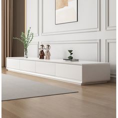 a living room with white walls and wooden floors, two vases on top of the entertainment center