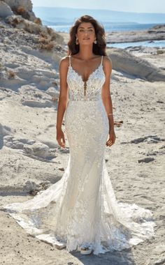 a woman standing on top of a sandy beach wearing a wedding dress with an open back