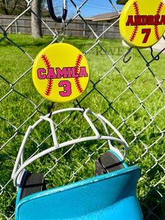 some baseball buttons are hanging on a chain link fence in front of a grassy field