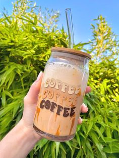 someone holding up a coffee cup in front of some trees and bushes with the words coffee on it