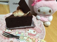 a plate with a piece of chocolate cake on it and a hello kitty doll next to it