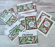 four christmas cards with holly and berries on them, sitting on a wooden table next to each other