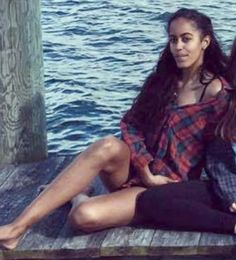 two young women sitting on a dock next to the water with their arms around each other