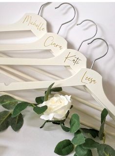 three white wooden hangers with names on them and flowers in the foreground next to each other