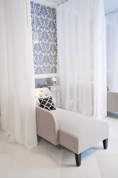 a white couch sitting in front of a window next to a wall with curtains on it