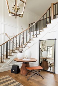 a room with stairs and a mirror on the wall, in front of a table