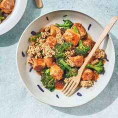 two bowls filled with rice and vegetables on top of a blue tablecloth next to wooden utensils