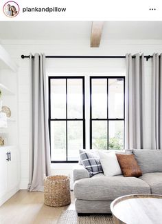 a living room filled with furniture next to a window covered in gray curtains and pillows