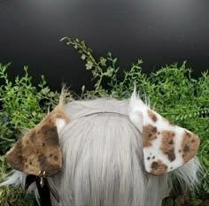 the back of a white and brown horse's head with leaves on top of it