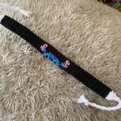 a black and blue beaded wristband laying on top of a white rug next to a pair of scissors