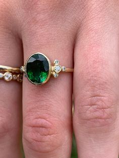 A perfect emerald green Tourmaline is set in Emily's 14k gold Trefoil cluster setting with a freeform band. We originally saw this as being a unique engagement ring but it would be just as wonderful as an everyday bit of sparkle and looks phenomenal with our halo bands Approximate stone size: 10mm x 8mm TCW tourmaline: 2.5ct TCW diamonds: .12ct Mohs Stone Hardness: 7.5-8 This one of a kind piece is handmade in Emily's Hudson Valley studio. If you have questions about sizing, shipping or need hel Oval Green Rose Cut Diamond Rings, Green Emerald Cluster Ring With Rose Cut Diamonds, Green Cluster Ring With Rose Cut Diamonds, Green 14k Gold Cluster Ring, Oval Tsavorite Ring With Bezel Setting, Unique 14k Gold Green Emerald Ring, Unique 14k Gold Emerald Ring, Unique Green Emerald Ring In 14k Gold, Unique Green Emerald 14k Gold Ring