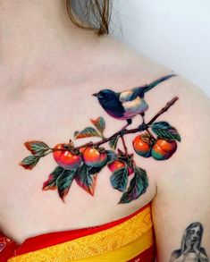 a woman with tattoos on her shoulder and chest is holding an apple tree branch in front of her