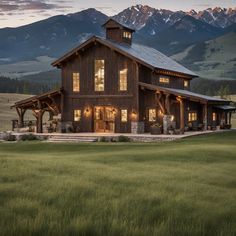 a large wooden building sitting on top of a lush green field with mountains in the background