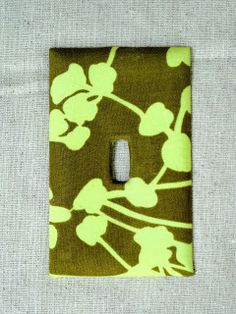 a green and white flowered light switch plate cover on a gray cloth wallpaper