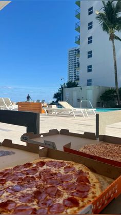 two pizzas sitting on top of boxes next to each other in front of a swimming pool