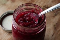 a jar filled with red liquid sitting on top of a wooden table next to a spoon