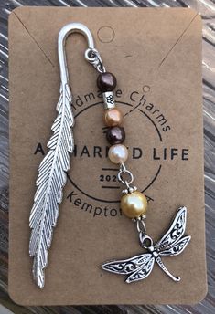 a silver charm with a dragonfly and pearl bead on it's end