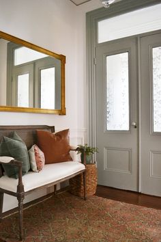 a bench with pillows on it in front of a door and mirror over the doorway