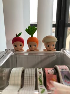 three small plastic carrots sitting on top of a shelf next to rolls of tape