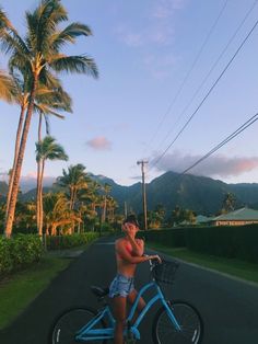 a man riding a blue bike down a street with palm trees in the back ground