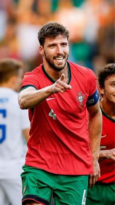 a man in red shirt and green shorts standing next to another man with his hand out