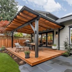 a patio with a table and chairs under a pergolated roof in front of a house