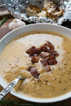 a white bowl filled with soup on top of a wooden table next to silver foil