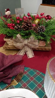 a wooden box filled with pine cones and red berries on top of a green table cloth