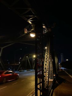 a red car driving down a street next to a tall metal structure with lights on it