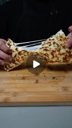 a person holding a piece of pizza on top of a wooden cutting board