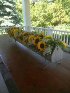 sunflowers and other flowers are arranged in a planter on the porch