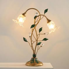 a lamp with three lights on top of it and green leaves growing out of the base