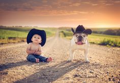 a baby sitting on the ground next to a dog wearing a cowboy's hat