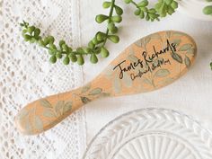 a wooden spoon sitting on top of a glass plate next to some green leaves and flowers