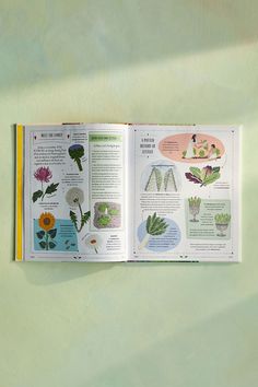 an open book with pictures of flowers and plants on the pages, sitting on a green surface