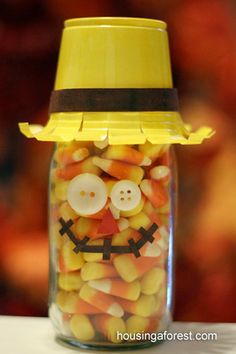 a glass jar filled with candy corn and a smiley face on the lid that has buttons in it