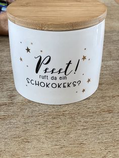 a white ceramic container with gold stars on it and a wooden lid that says pet i put da ol chokokeks?