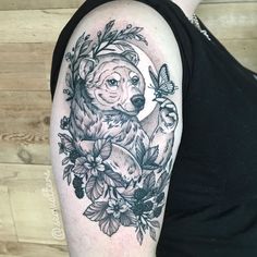 a woman's arm with a bear and flowers tattoo design on the left upper arm