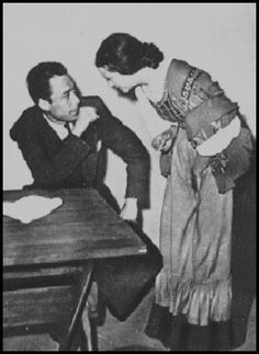 an old black and white photo of two people sitting at a table with one person touching the other's head