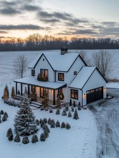 a large white house covered in snow with trees and lights on the front porch, surrounded by evergreens