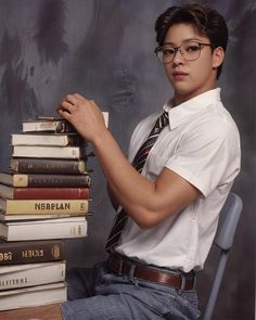 a young man sitting in front of a stack of books