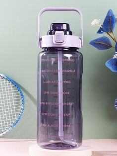 a purple water bottle sitting on top of a white table next to a tennis racket