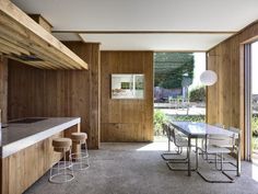 an open kitchen and dining room area with wood paneling on the walls, concrete counter tops, and bar stools