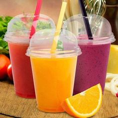 three cups with straws and orange slices on a wooden table next to some vegetables