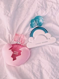 two perfume bottles sitting on top of a bed next to an object shaped like a heart