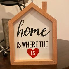 a wooden frame with the words home is where the heart is on top of a table