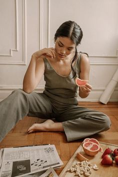 a woman is sitting on the floor with fruits and nuts in front of her as she eats