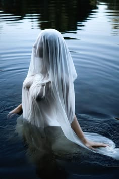 a woman is floating in the water with her veil over her head and dress on