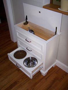 a white dog house with two dogs bowls on the bottom and one in the middle